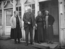 Tre kvinnerb og en mann står ved inngangspartietr til et hus