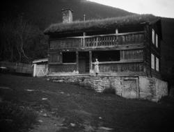 Tømmerhus med svalgang og torvtak. En kvinne ved inngangen.