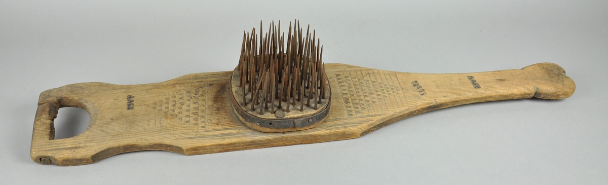 Linhekle av tre med håndtak i den ene enden og den andre enden er smalere enn resten av brettet. Brettet har skjellutskjæringer og inskripsjon, og på midten en avrundet kloss med stålspiker .