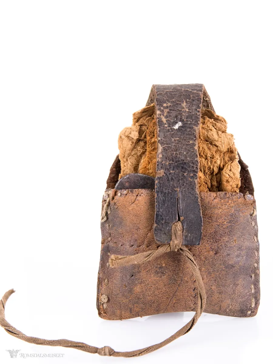 Fyrtøy bestående av en liten lærpose, slagstål, flint og knuskstykker. I posen er det to knuskstykker. Slagstålet har nærmest strykejernsform.