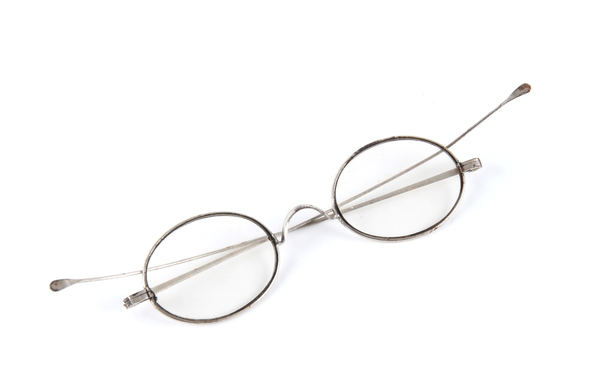 Brille med ovale glass. Tynn metallinnfatning med hengsler og to stenger.