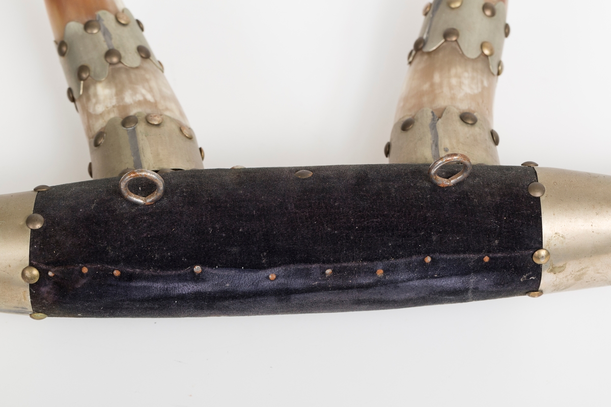 Knaggrekke antagelig håndlaget av kuhorn. 4 horn/kangger. Montert med "dekorative" beslag som er spikret og dekornaglet på hornene. Kledd med cordfløyelstoff på midtparti. To øyeskruer på toppen for feste til vegg.