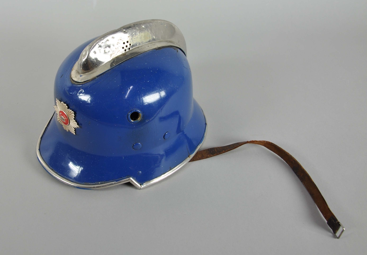 Blå brannhjelm av metall. Hjelmen har innerhjelm og hakereim av lær. På toppen er går det en opphøyd kant eller hanekam. På framsiden er emblem for det norske brannvesenet.