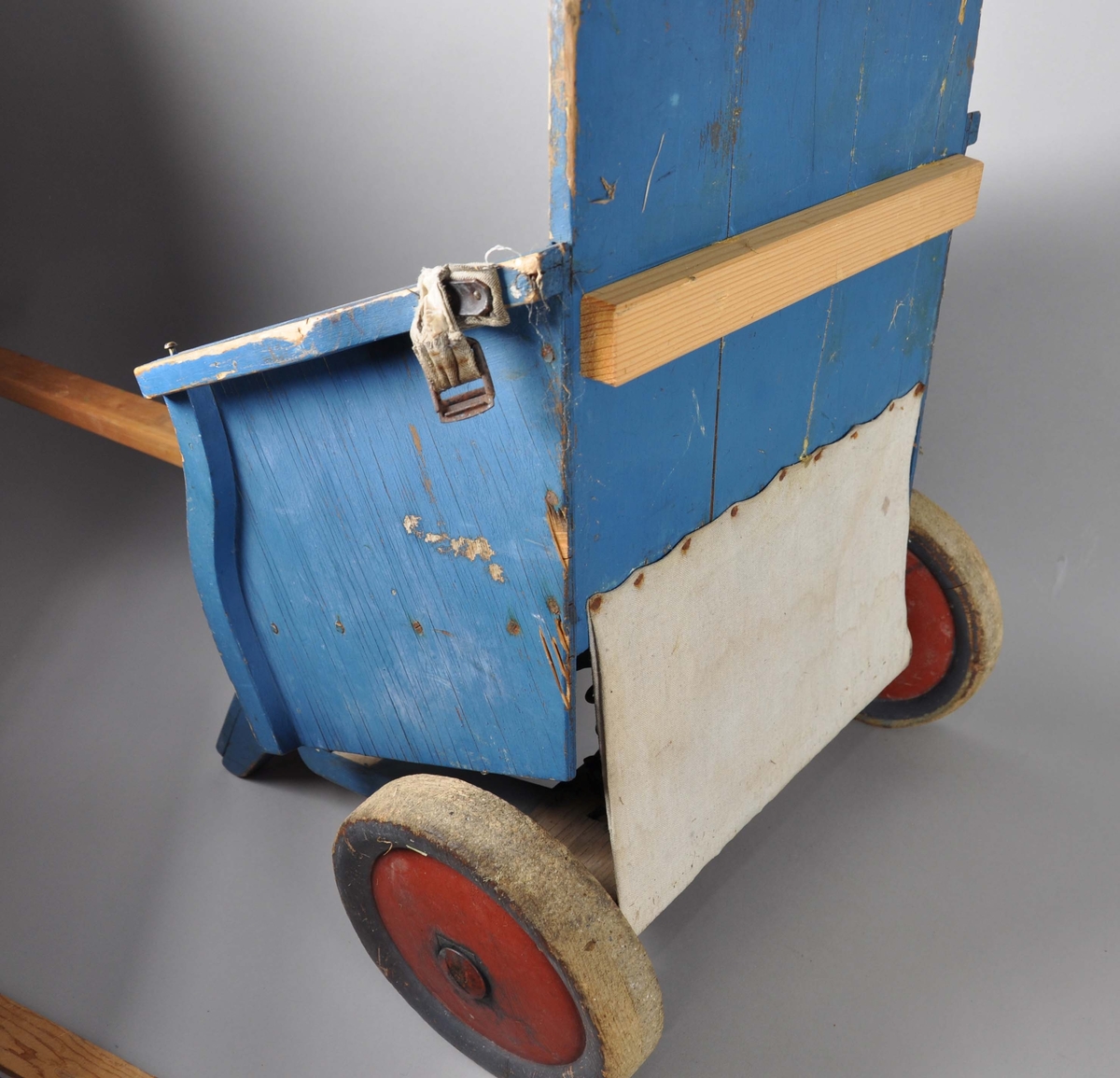 Håndlaget trilleav tre. Består av sete på to hjul, lærreim til belte, fotstøtte og draspak. Hjulene er av tre, og kapslene er malt røde. Setet står på to fjæringer fra madrass. Nederst på fotstøtten mangler det en oppstående list. Malingen er noe avslitt. Draspaken er trehvit og kan være erstattet i nyere tid.