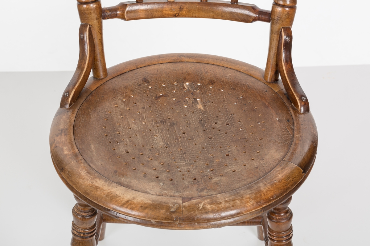 Stol i lakket treverk. Rundt stolsete med hullemønster. Rygg som er svakt buet med spiler og mønster. Dreide ben om spiler i rygg.