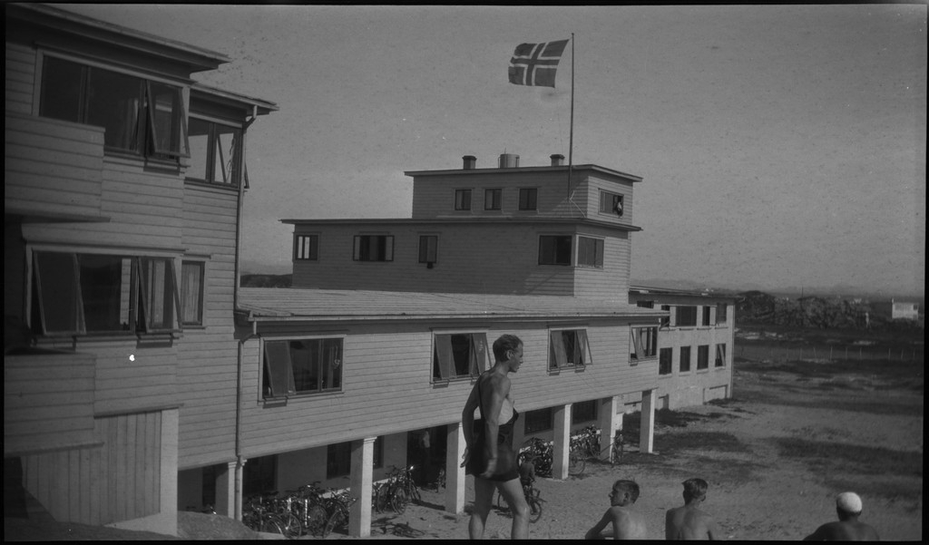 En stor vennegjeng i lystig lag på stranda på Sola. De har trommer og trekkspill og leker i vannet og på land med og uten ball. Sola strandhotell ligger i bakgrunnen. Tor Johannessen og Harald Bergsaker er på bilde nr. 14 og 18.