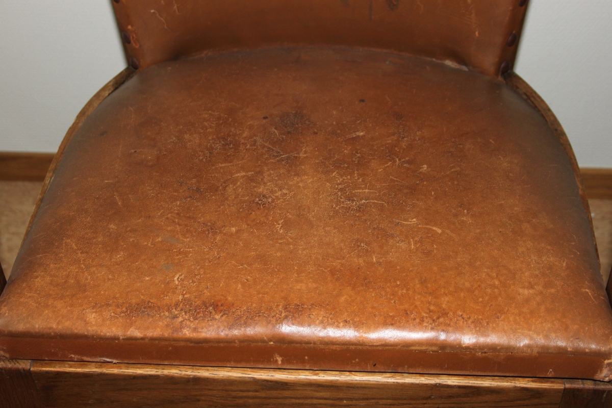 Møteromstol/kontorstol med armlener samt buet rygg. 4 ben. Metallbeslag under armlener. Brunt skinn i rygg og sete. Stolen er lakket med klar lakk. Originalt møbel innkjøpt til det nye Statsarkivet i Kristiansand i 1935.