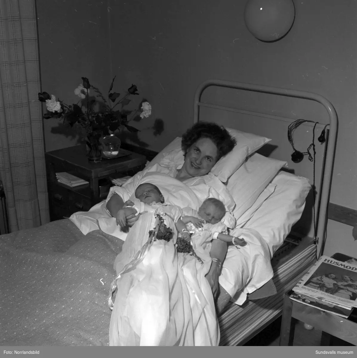 En familj på Sundsvalls BB med mor, far och ett nyfött tvillingpar. Barnen är klädda i dopklänningar.