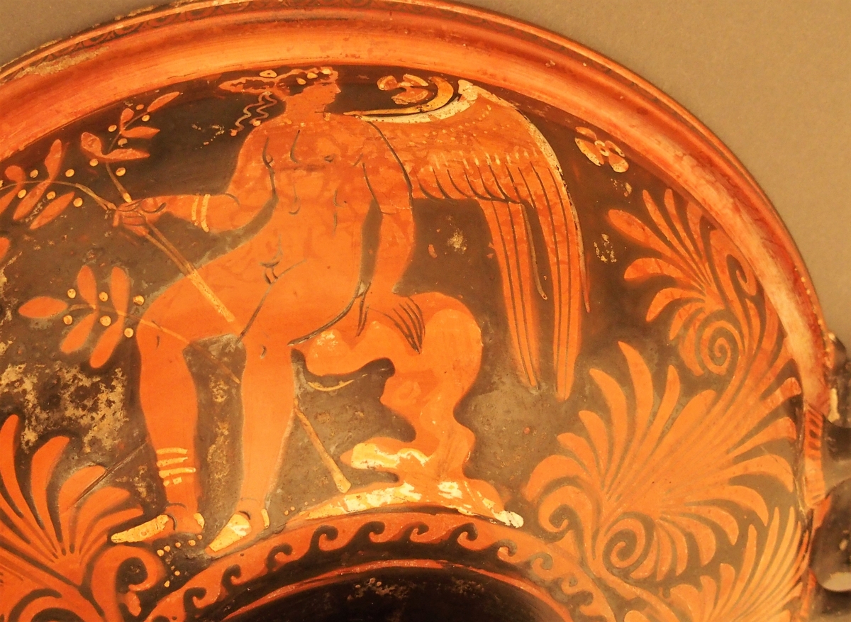 I skålens bunn naken mann (Dionysos) og kvinne med tamburin (mænade). Under dem en eggstav (kymation). Motivet er omgitt av løpende hund i sirkelform. På hankene hare og fugl. På undersiden palmettfrise (anthemion),løpende hund, mænade med tamburin og tromme og naken mann med olivengren (Apollon).