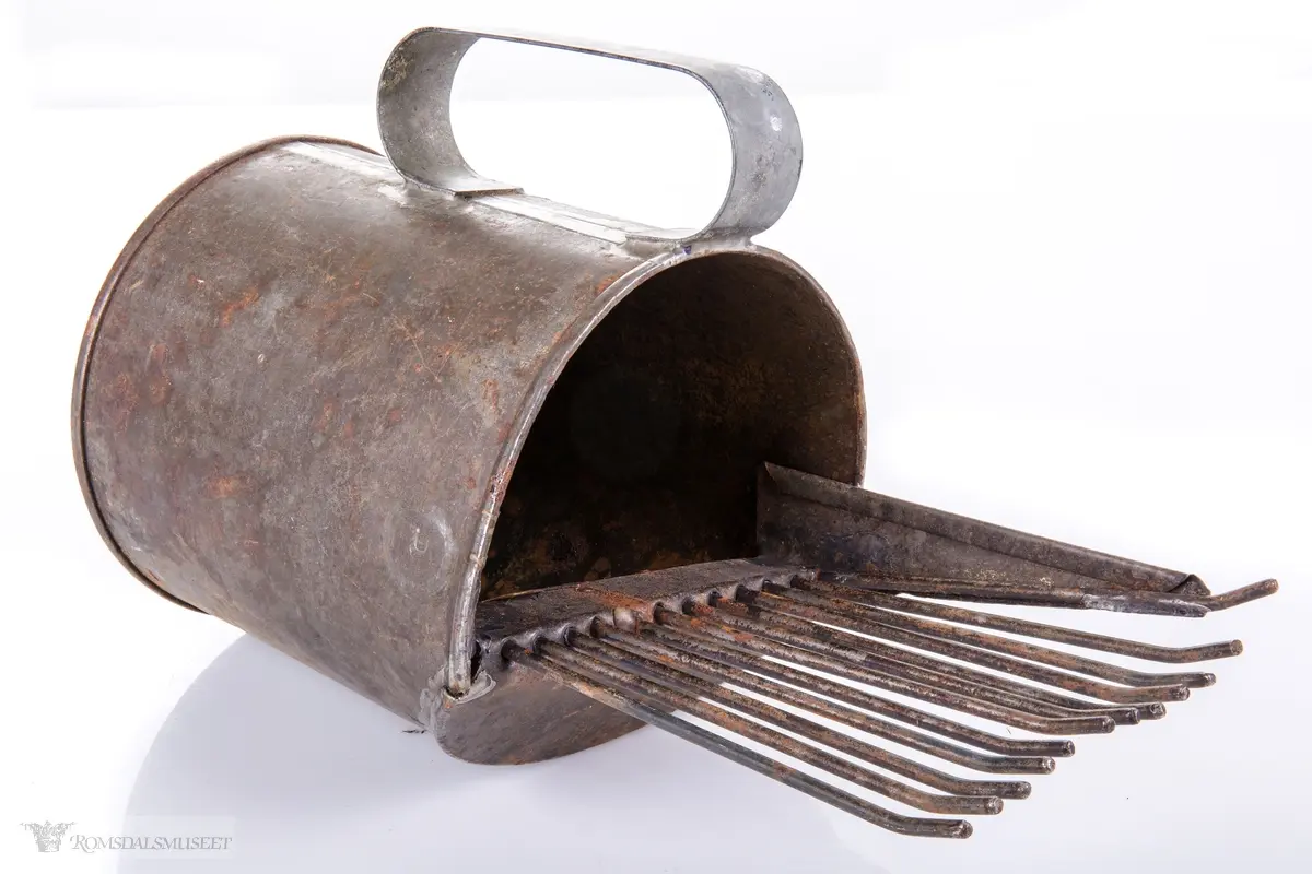 Sylinderformet blikkboks som kropp, med påloddet buehåndtak og en skråstilt plate med tenner foran.