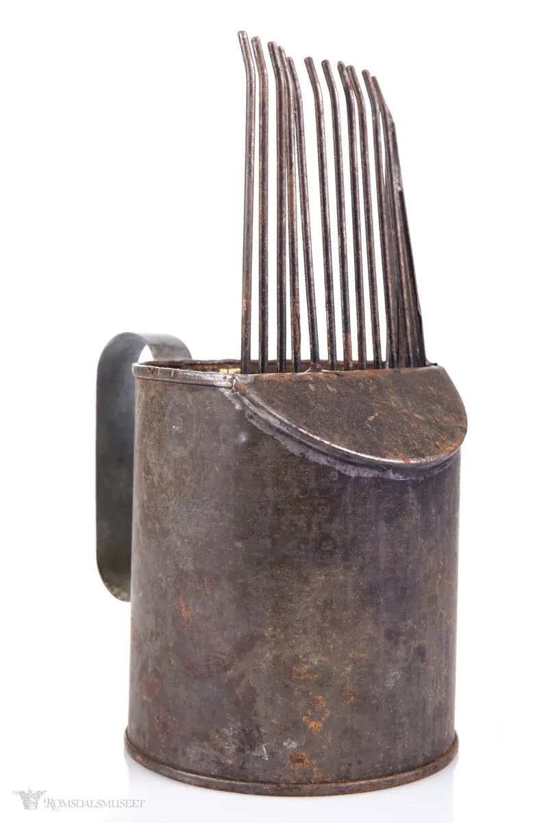 Sylinderformet blikkboks som kropp, med påloddet buehåndtak og en skråstilt plate med tenner foran.