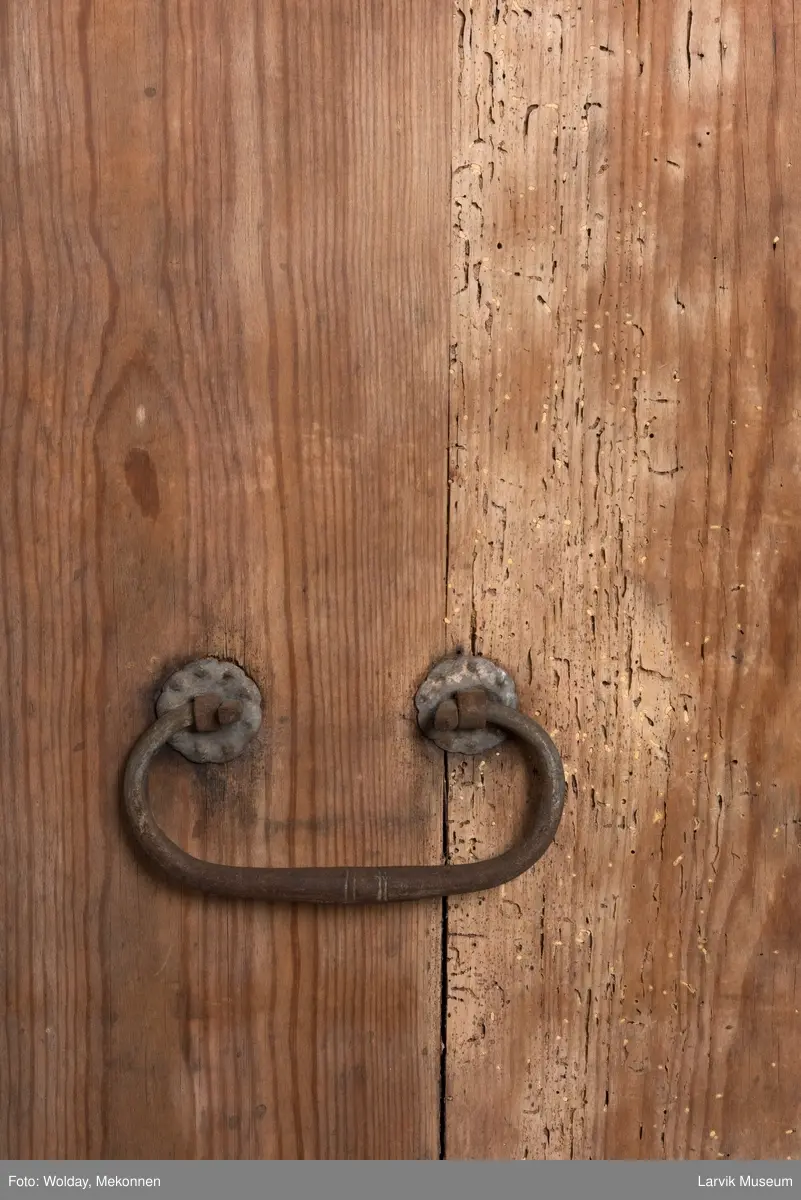 Kommoden har 4 skuffer. 2 beslag for å dra ut, 1 beslag for nøkkelhull, messing. Utskåret dekor under øvre pyntelist "tanngard" rundt på 3 kanter. Øvre skuff utskåret med bølgebånd med rett linje som bryter bølgene. Utskjæring kun i front. To av kommodens hjørner har utskåret søyle. Håndtak på kortsidene for å bære i.