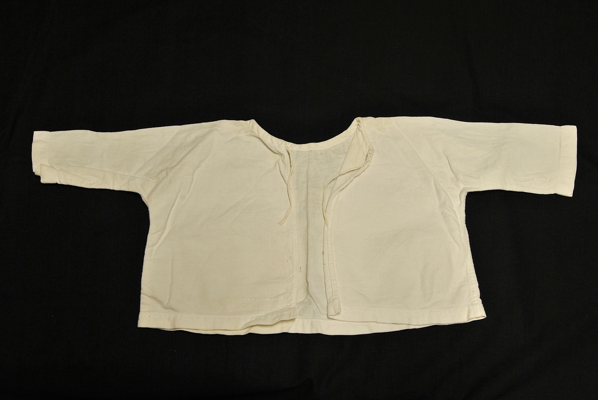 Undertrøye til spedbarn. Rektangulær i formen. Knytinger bak.