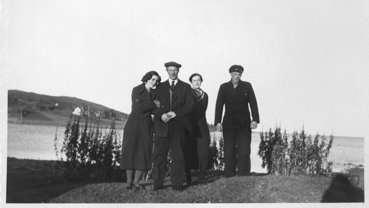 Fire kvinner og menn, fotografert ute med hav og bebyggelse i bakgrunnen.