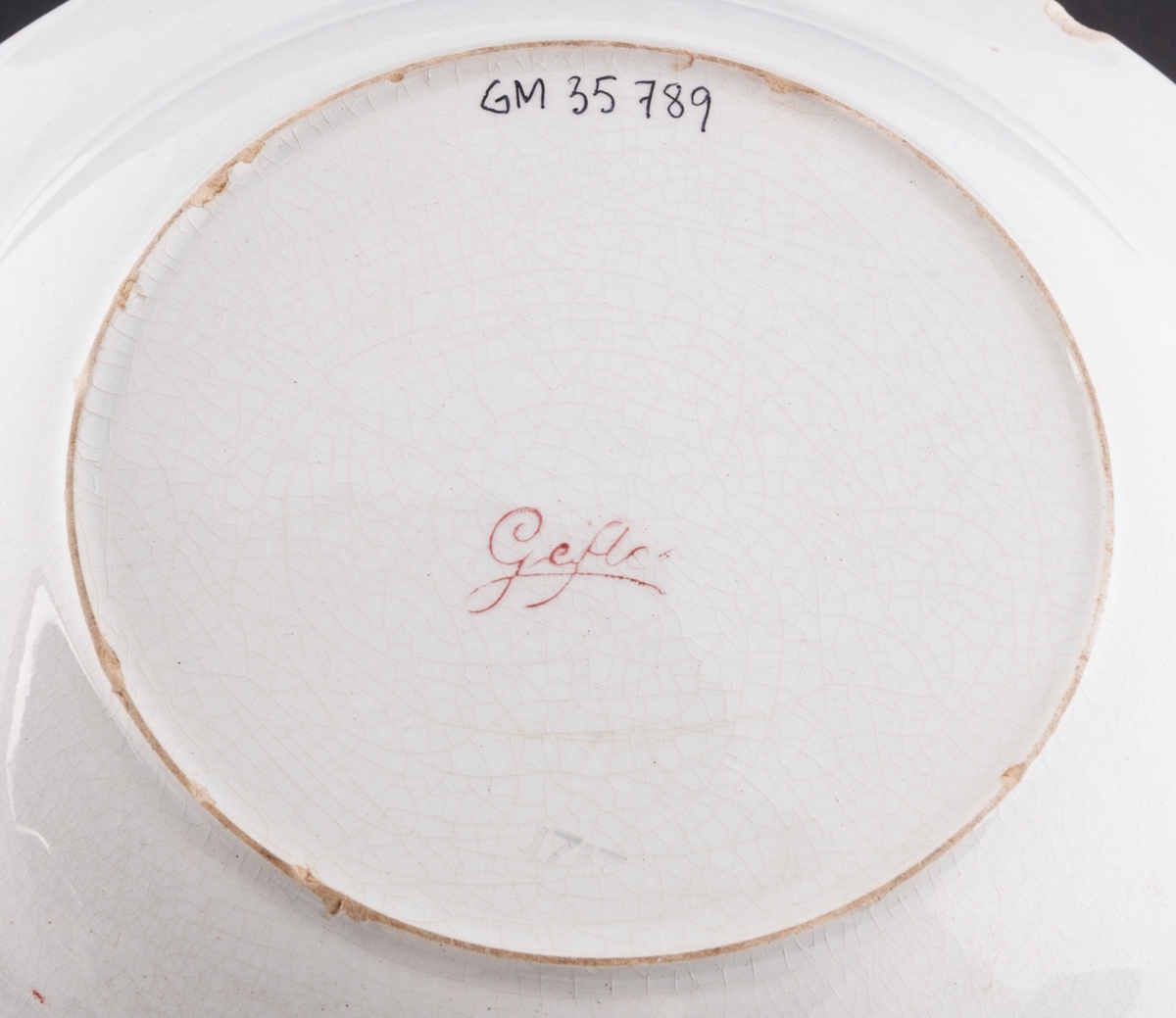 Djup mattallrik tillverkad vid Gefle Porslin AB på 1910-talet. Försedd med tryckt mönster, överföringsbilder i form av tomtemotiv på brämet. På undersidan stämplat "Gefle".