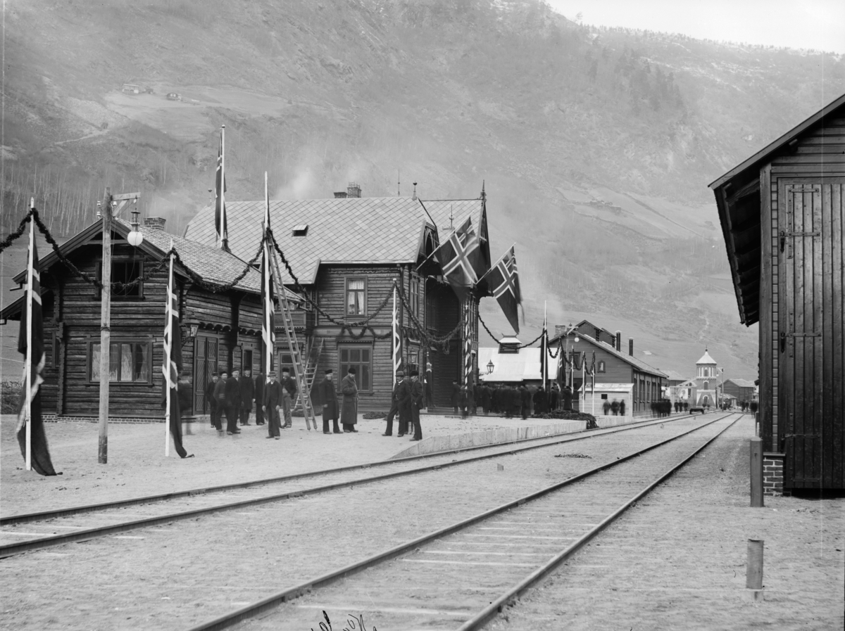 Otta stasjon pyntet for åpning 29. oktober 1896. Til venstre for stasjonen vise vognremisset/lokomotivstall, vanntårnet og til høyre godshuset. Mange personer på perrongen (som venter på toget)