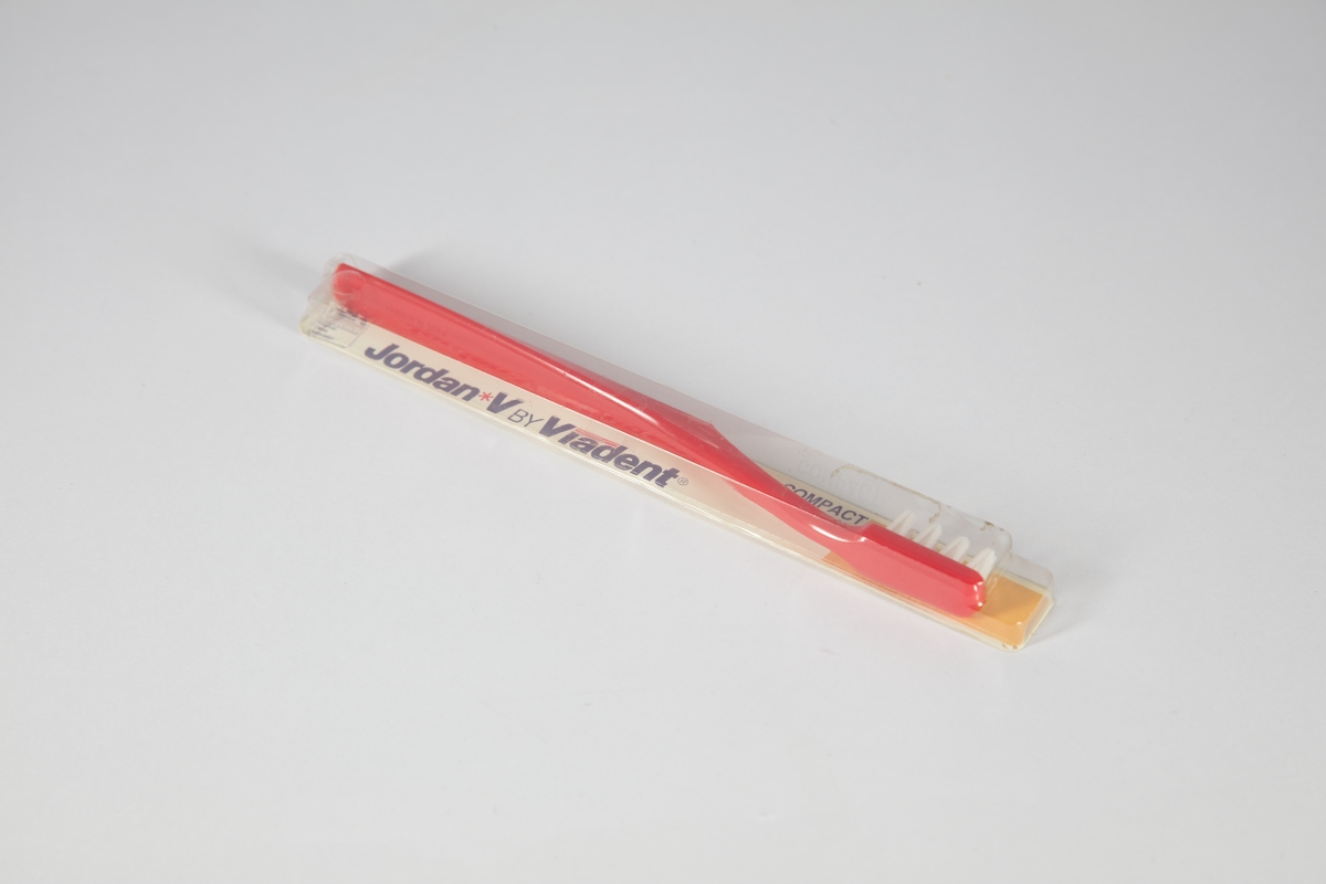 En rød tannbørste som ligger inni uaåpnet emballasje.