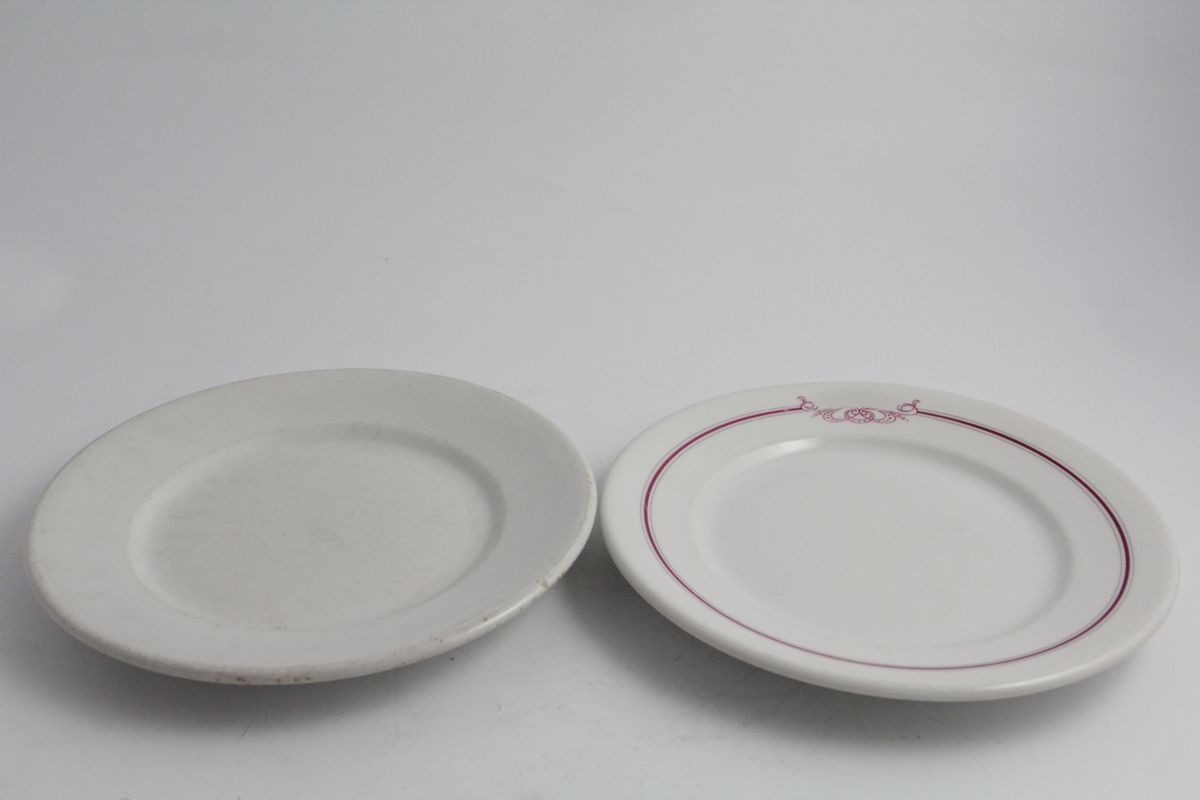 To runde tallerkener, ulike. A er hvit, uten dekor. B har hvit bunn, burgunderrød kant på fane, sløyfeornament og utraderte bokstaver.