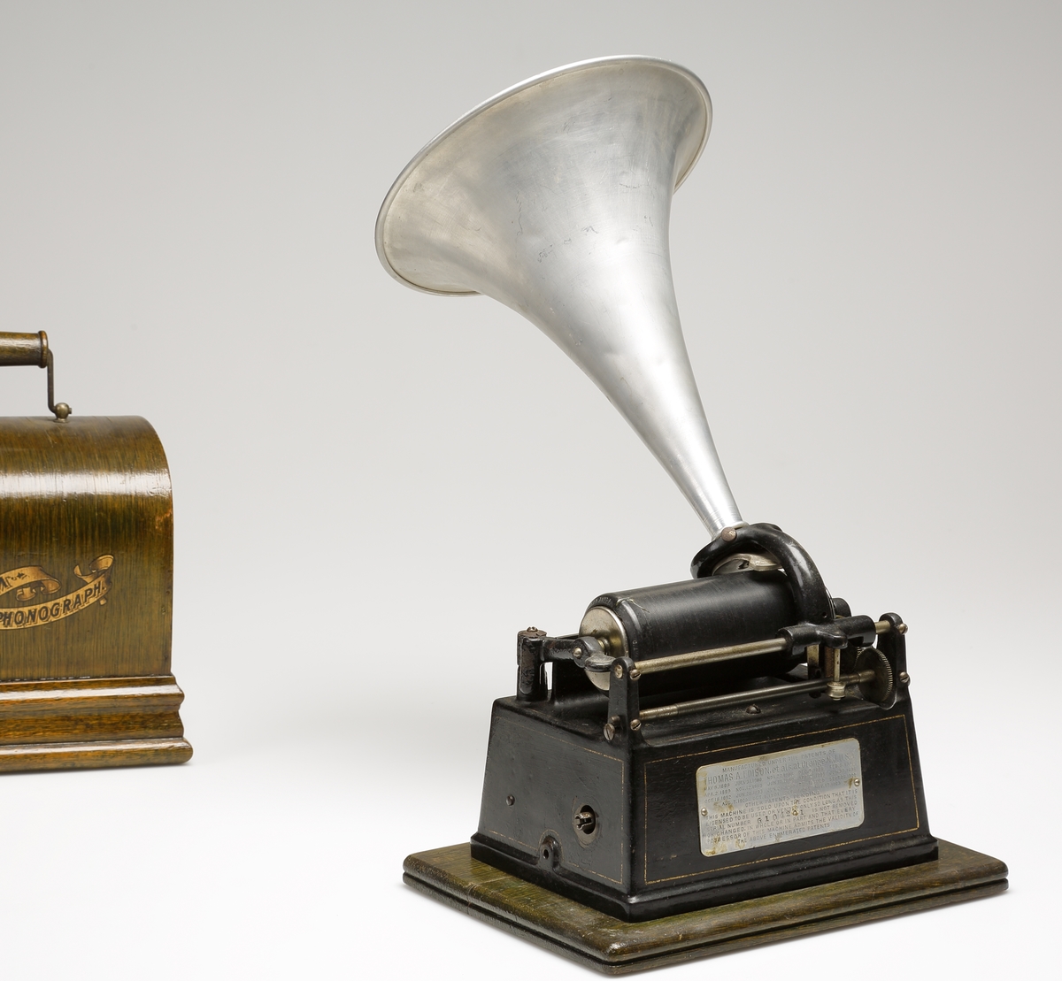 Fonograf, med förvaringslåda. 
Rektangulär, svartlackerad metallåda med musikinstrumentet ovanpå. Dessutom en förnicklad (?) tratt. Vrides upp med nyckel på kortsidan. 
Förvaringslåda av fernissat trä med handtag och påmålad text: "Edison, GEM, Phonograph".