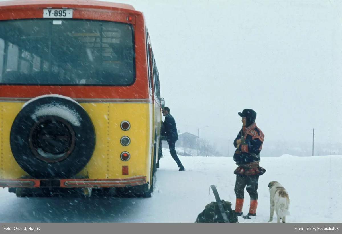 Rutebussen utenfor butikken i Masi (Máze på samisk) på 1970-tallet. Det er vinter og bussen tar med seg posten innsamlet av postfører Mathis Mathisen Buljo og bringer den videre. En passasjer i kofte, med ryggsekk, ski og trekkhund står utenfor bussen (Se også FBib.10001-285).

Bussen er registrert Y-895. Det var en Volvo B57, karosseri bygd hos Vestfold Bil og Karosseri (VBK), Horten, 1969-modell. Eier av bussen var Finnmark Fylkesrederi og Ruteselskap (FFR) og den er lakkert i selskapets karakteristiske farger, skarp gul og rød. 

Fotograf Henrik Ørsteds bilder er tatt langs den 30 mil lange postruta som strakk seg fra Mieronjavre poståpneri til Náhpolsáiva, videre til Bavtajohka, innover til øvre Anárjohka nasjonalpark som grenser til Finland – og ruta dekket nærmere 30 reindriftsenheter. Ørsted fulgte «Post-Mathis», Mathis Mathisen Buljo som dekket et imponerende område med omtrent 30.000 dyr og reingjetere som stadig var ute i terrenget og i forflytning. Dette var landets lengste postrute og postlevering under krevende vær- og føreforhold var beregnet til 2 dager. Bildene gir et unikt innblikk i samisk reindriftskultur på 1970-tallet. Fotograf Henrik Ørsted har donert ca. 1800 negativer og lysbilder til Finnmark Fylkesbibliotek i 2010.