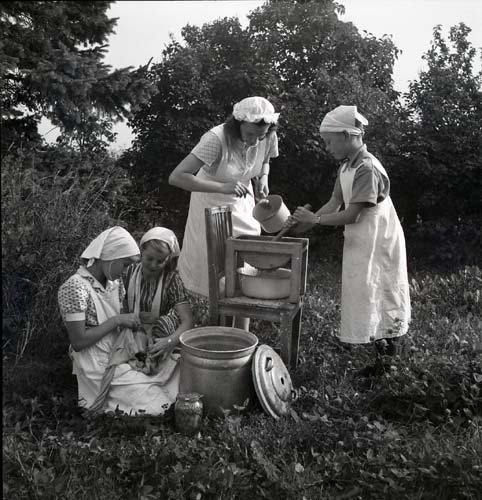 En kvinna och några barn står utomhus och arbetar med konservering och att göra äppelmos. Från Unga Odlares klubbodlingar, 1948.