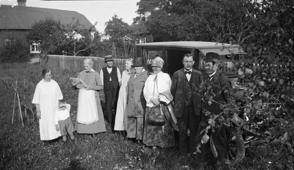 Tora och Tore Alinder med flera personer framför bil i trädgården i Sävasta, Altuna socken, Uppland 1927