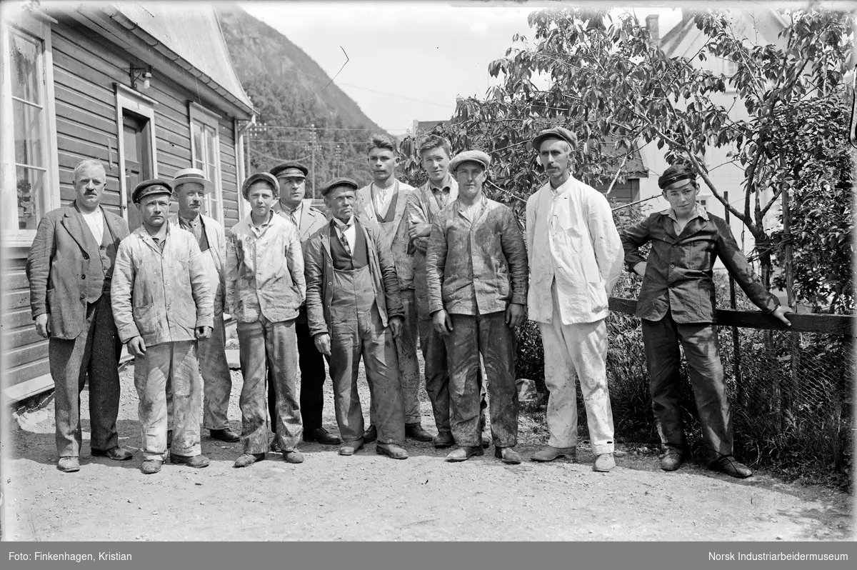 En gruppe menn i arbeidsklær utenfor bolighus på Rjukan.