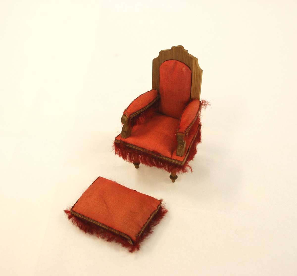 Dukkemøblement 9 deler: 
A) Sofa i rødt silke på setet, rygg og armlener (lener med pøller). Høy rygg med utskjært toppgavl i tre. Røde frynser nederst i fronten, på sidene og røde dusker på pøllene. 
B) Lenestol med frynser i front på sidene og på armlenene. Høy rygg med rødt silke på setet, ryggen og armlener. 
C) Stol med rødt silke på setet og røde frynser rundt stolsetet. Dreide forben, høy, svunget rygg med løvsagarbeid.
D) Bord i tre med avrunede sider, fire freide ben hvorav et ben er surret øverst i hvit bandasje. 
E) Konsollspeil med marmorplate og gavl med trespir med fire lave kuleføtter. Speil med utskjært treramme. Dreide ben fra marmorplaten ned til understellet.
F) Fotkrakk i rødt silke med røde frynser rundt hele. Nederst er fire lave kuleøftter.