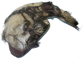 Bindmössa vars yttertyg är nästan helt borta. Foder av linne vävt med tuskaftsbindning, mellan linnefodret och resterna av övertyget syns linnefibrerna som ligger emellan som fyllnad. Kantad med ett blått sidenband.