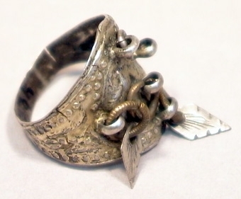 Fingerring av förgyllt silver med utvidgat framstycke på vilket fem ringförsedda öglor är fastlödda. I öglorna sitter rombformade små hängen, två stycken finns kvar av fem ursprungliga. På ringen finns driven ornering.
