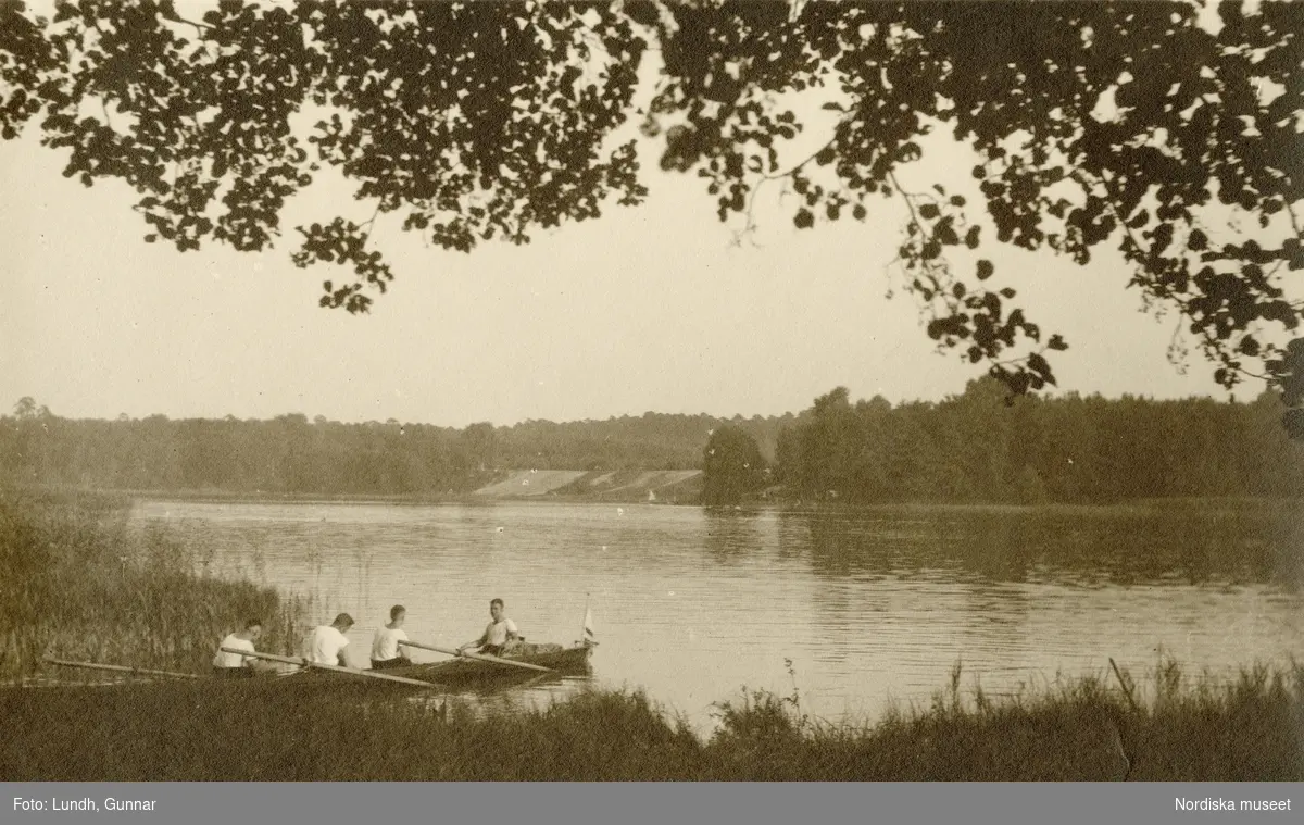 Tyskland. Fyra unga män i en roddbåt i strandkanten vid en sjö.