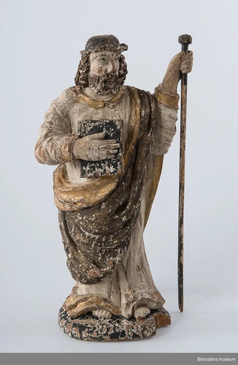 Träskulptur, apostelbild från 1600-talet som tilhör altartavla UM000393.  Förgyllningen som uppvisar båda bladguld, slagmetall och/eller silver.
UM000395a = själva skulpturen,  UM000395b = skulpturens lösa stav.

Enligt katalogkort föreställer skulpturen helgonet och aposteln Jakob den äldre; tillhör altaruppsats UM000393a-i.
Vandringsstaven brukar attribueras till Jakob den äldre.
Krederat trä med mager oljefärg och oljeförgyllning. 

Ur handskrivna katalogen 1957-1958:
Apostelbild, Lane Ryr
H. 39 cm; höger hand håller en bok, vänster en stav b) L. 39,5 cm. Färgen delvis flagn.; små bitar avslag.

Lappkatalog: 13

Se foto på föremålet i Uddevalla museums kyrkliga utställning 1920, UMFA53292:0013

Ur Nationalencyklopedin, NE.se:  Apostel
I konsten framställs apostlarna alltid barfota samt klädda i tunika och mantel. De bär oftast en bok samt sitt individuella attribut, i allmänhet respektive martyrredskap (Petrus bär dock himmelrikets nycklar).