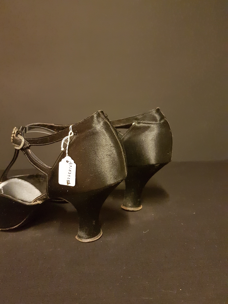 Ett par aftonskor i svart siden, klack, t-sleif spänne med meanderbård samt ett skospänne bestående av en ring med strasstenar.