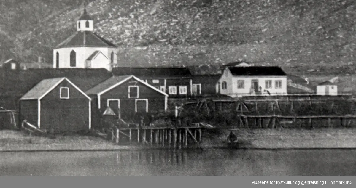 Handelstedet Kjelvik med kai, bolig, pakkehus og fiskehjeller. Kjelviks gamle åttekantete kirke (1844-1882) i bakgrunnen. Før 1882.