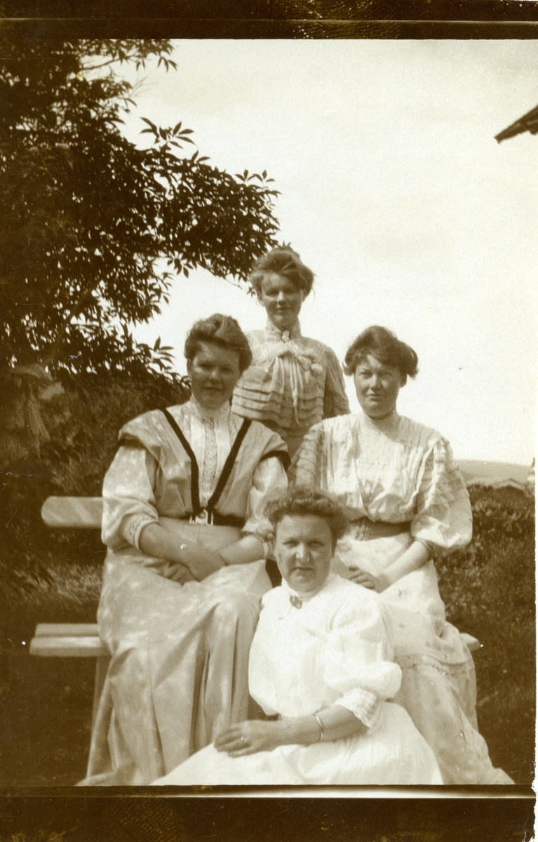 Gruppebilde av fire kvinner som sitter/står ved en benk.