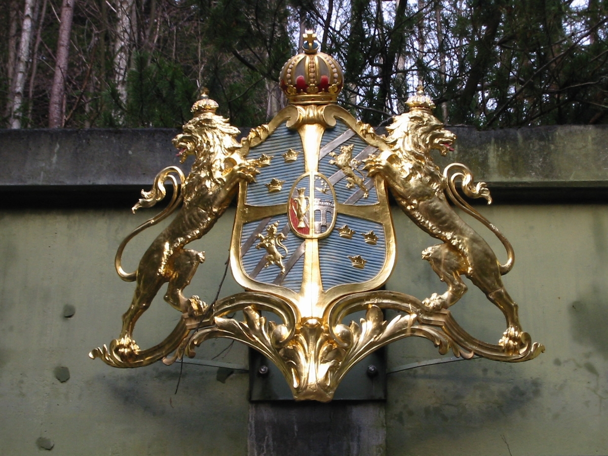 Akterskeppsornament från pansarkseppet TAPPERHETEN. Gjutet i mässing och bemålat. Föreställande stora riksvapnet, krönt med kunglig krona och flankerat av två lejon.