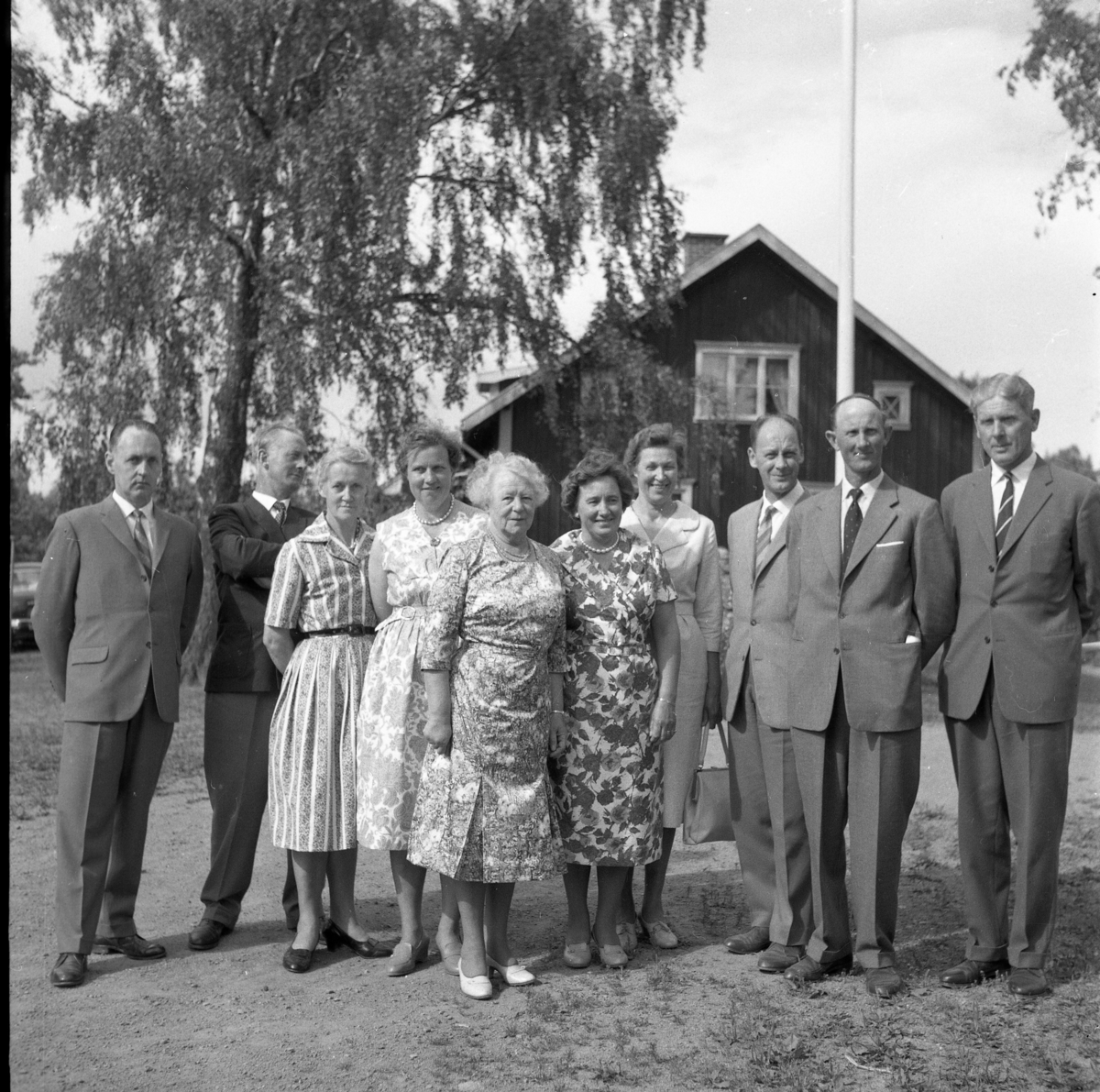 Skolträff i Reaby 1962. Kvinnor och män uppställda på skolgården framför en flaggstång, fr v: okänd, Nils Karlsson, Elvina Bjerkhed, okänd, Ruth Pettersson samt okända. Mannen till höger är Sven Rickardsson.