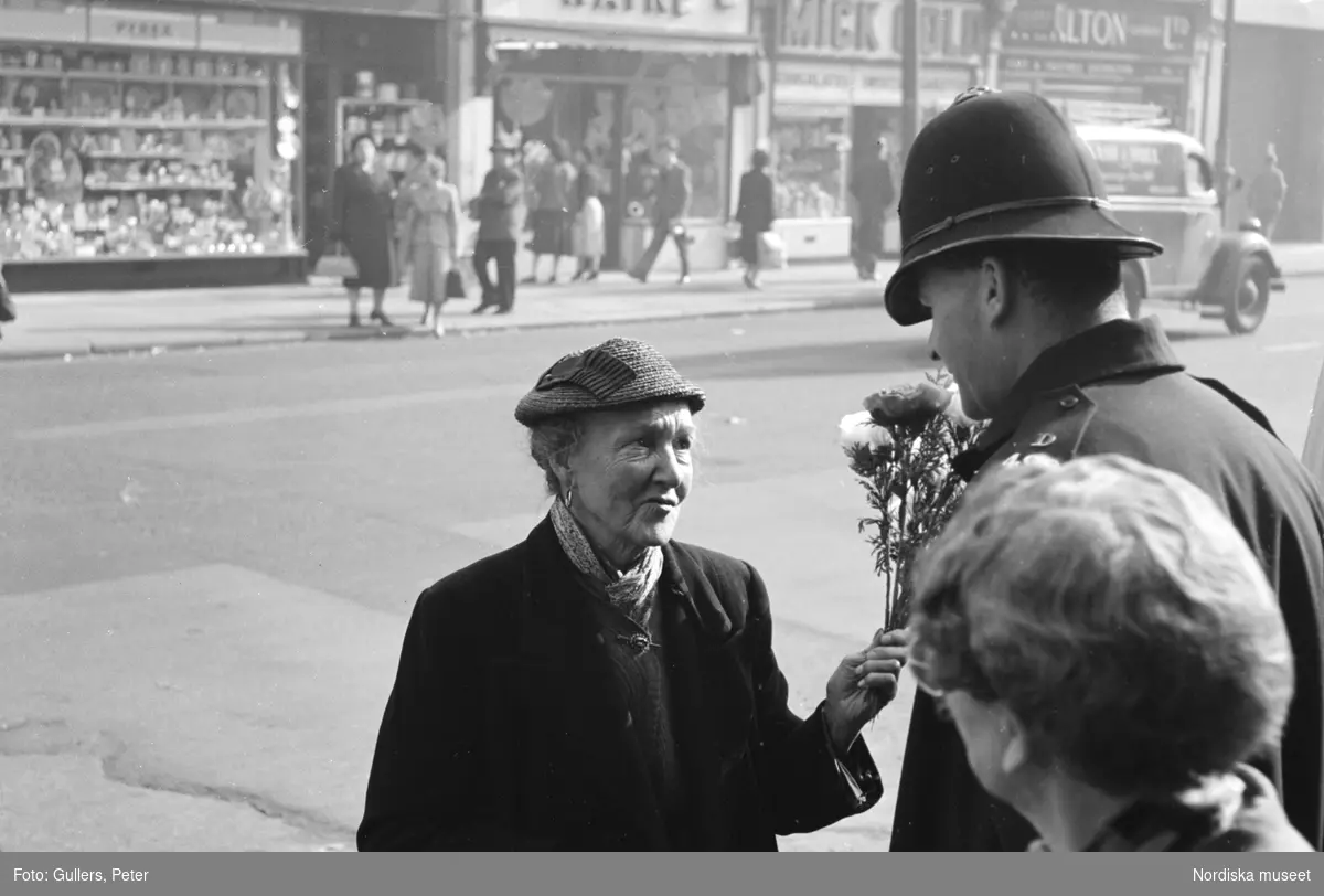 London, Camden High Street. En äldre dam med en blomsterbukett i handen samtalar med en polisman.
