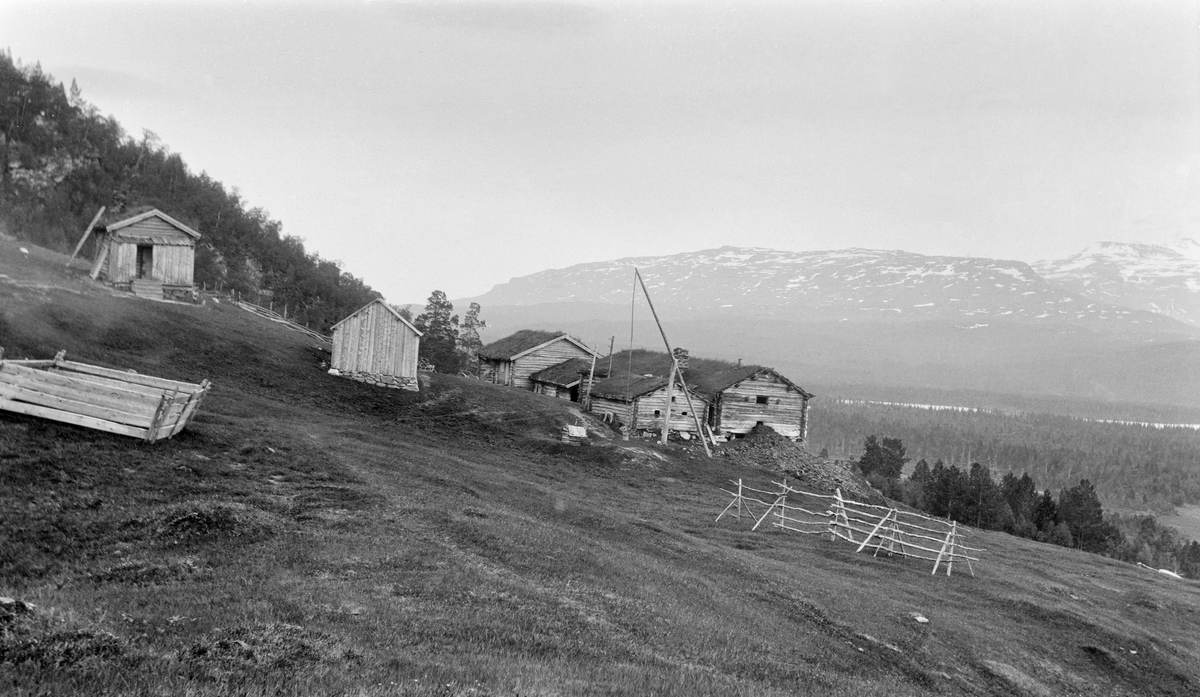 Bebyggelse på eiendommen Solvoll i Målselv kommune i Troms.  Fotografiet er tatt fra en grasvoll, der det åpenbart ble dyrket fôr til krøttera på garden.  Vi ser ei rajehesje til høyre i bildeflata og ei lita kve til venstre.  Den dominerende husklynga på bakkekammen sentralt i bildet er laftete uthusbygninger, antakelig et par fjøs, stall og løe.  Foran disse ser vi ei brønnvippe.  Til venstre i bildet, noe høyere oppe i bakken ser vi et par andre bygninger.  Den ene var antakelig et uthus utført i bordkledd bindingsverk, den andre (lengst til venstre) kan ha vært et våningshus.