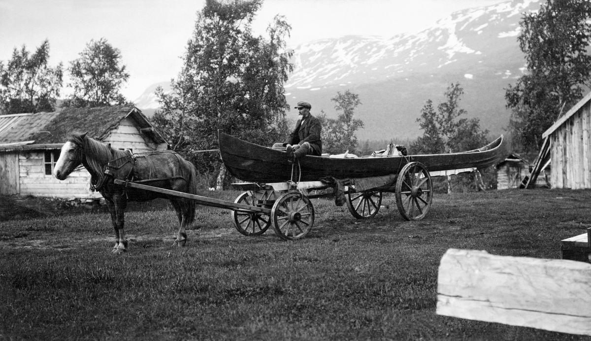 Båttransport med hest og vogn i Nordreisa statsskoger i Troms.  Fotografiet er tatt i gardstunet på eiendommen Potka i Reisadalen.  Et par hus skimtes lengst til høyre og venstre i bildeflata, men hovedmotivet er en hest som er forspent ei firehjulet tømmervogn der det er montert en lang, smal elvebåt.  Kusken, skogvokter Johannes Skjønsberg, sitter foran i båten med tømmene i hendene.  Vogna med båten trekkes av en lysebrun hest med hvitt bless i panna.  I bakgrunnen en fjellrygg med snø i revnene.  På uthusbygningen til venstre i bildet later det til at det foregikk taktekkingsarbeid da dette fotografiet ble tatt.  Til høyre ser vi ei torvtekket takflate, til venstre for den ei takflate som var pålagt fuktsperre av never, og lengst til venstre undertaket av bord. 

Johannes Olsen Skjønsberg var født på garden Mælum i Øyer i Gudbrandsdalen (Oppland fylke), der foreldrene hans var tjenestefolk.  Sjøl kom han til Skjervøy i Nordreisa i Troms, hvor han i 1885 fikk dattera Thora Josia med Stine Katrine Jensdatter.  De to giftet seg seinere samme år, og fikk barna Claudia Østine (1887), Sigurd Olkvart (1890), Margit Fernanda (1892) Alma Olia Vanbora (1895) og Karley Vedevang Løvenskjold (1899), samt pleiedattera Dagny (f. 1901).  De fleste av barna ble født på eiendommen Samuelelv, som var fødestedet til skogvokterens kone.  I 1900 oppgis Tømmernes (gnr. 18, bnr. 9) som bosted for familien, i 1910 bodde de på en eiendom de kalte Skjønsberg (gnr. 26, bnr. 4). 