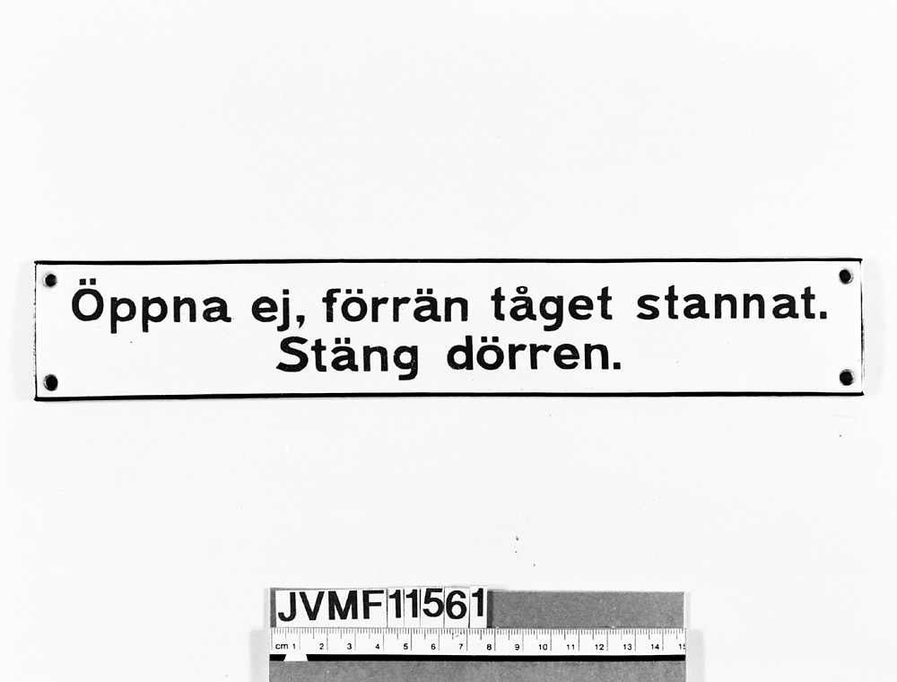 Rektangulär skylt av emaljerad plåt med brun text på vit botten: "Öppna ej, förrän tåget stannat.
              Stäng dörren".

Anm:
1: "Lika": Jvm 11559, 11556 ( ram eller tillst. skiljer).
2: Snarlika: Jvm 11709 - 10 (ålderdomligare, blå text, andra mått).
3: Snarlika: Jvm 11703, 11806 (blå text, samma mått och typsnitt).
