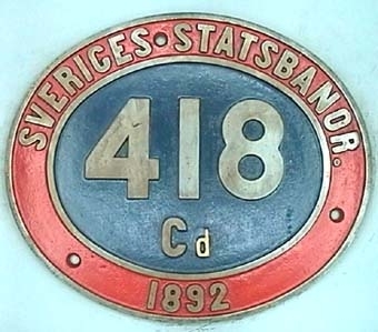 Oval skylt av mässing med text i relief mot blå botten och röd ring runt kanten.
Från ångloket SJ CC 418, Cd (1921).
NOHAB Nº 339.