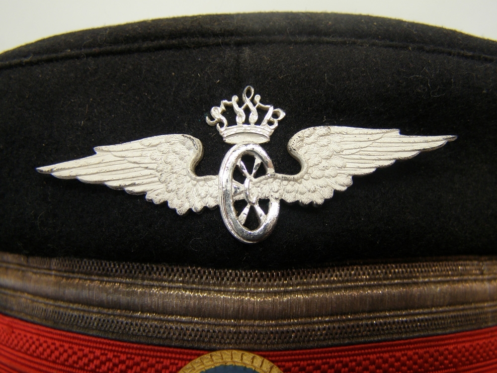 Skärmmössa av blåsvart kläde med jaquardvävt rött mössband, 13 mm silvergalon och vinghjul krönt av SWB-monogram, samt nationalkokard av metall, silverträns och silverknappar.