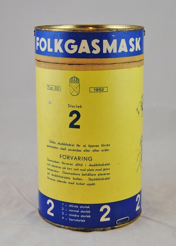 Skyddsfodral till gasmask, "folkgasmask", typ 32 Gullmaren. Skyddsfodralet är utformat som en pappcylinder med metallbotten och metall i  locket (Jvm 20327:3). I botten och locket sitter öglor för att kunna bära gasmasken i en rem. På framsidan av fodralet står det "Typ 32", vapensköld, "1952", "Storlek 2", "Detta skyddsfodral får ej öppnas förrän gasmasken skall användas eller efter order. FÖRVARING Gasmasken förvaras alltid i skyddsfodralet och placeras på torr och sval plats med jämn temperatur. Gasmaskens behållare placeras på skyddsfodralets botten. Skyddsfodralet förvaras stående med locket uppåt." På den blå kanten står det "1 - största storlek 2 - normal storlek 3 - mindre storlek 4 - barnstorlek". På andra sidan står det "BRUKSANVISNING Gasmasken påtages på följande sätt: 1. Håll andan. Tag av huvudbonad. 2. Tag upp gasmasken och fatta den med båda händerna på innersidan om det T-formade spännet. 3. Böj huvudet något bakåt och skjut hakan in i ansiktsskyddet. 4. Drag banden bakåt över huvudet tills de blivit sträckta. 5. Jämka ansiktsskyddets kanter så att de ligga slätt och tätt intill ansiktet och kontrollera att banden ej vridits. 6. Andas ut kraftigt och sedan lugnt och normalt. 7. Gasmasken avtages genom att man med båda händerna fattar i sidobanden, vilka sedan dragas över huvudet. Det är viktigt att gasmasken tillpassas riktigt. Anvisning härför finnes inuti detta skyddsfodral." På skyddsfodralet är det fyra bilder som visar hur gasmasken sättes över ansiktet.

Modell/Fabrikat/typ: Typ 32