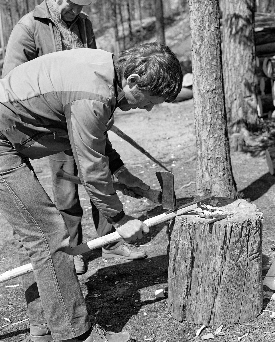 Skjefting av fløterhake, Stenbekk-koia, Trysilelva. Bildet er datert 22. 5. 1986. Her slås det inn ei nagle som skal feste haken til et nytt skaft. Arbeidet gjøres ved hjelp av hammeren på ei øks med en hoggestabbe som underlag.