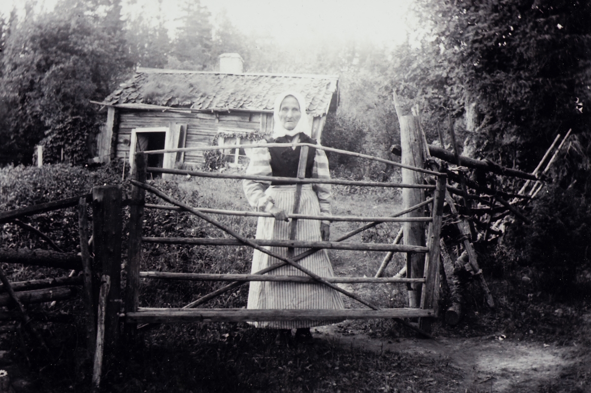 Anna Håkansdotter-Andersson "Jönsamora", Södra Jönsatorp, Svenshyttan.

En kvinna vid grinden. Bostadshus (torp) i bakgrunden.
Foto omkring 1905.
Se även bild OLM-2015-29-8