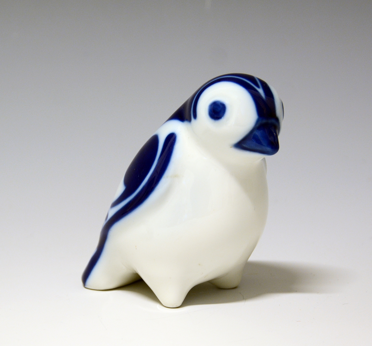 Liten fugl av porselen, med hvitt bryst, blå dekor på nebb og fjærdrakt.