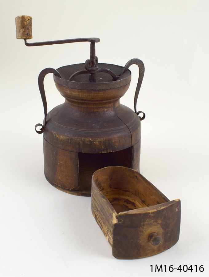 Kaffekvarn svarvad av trä. Kvarnen har två stycken S-formade handtag av järn. En utdragbar lucka nedtill.