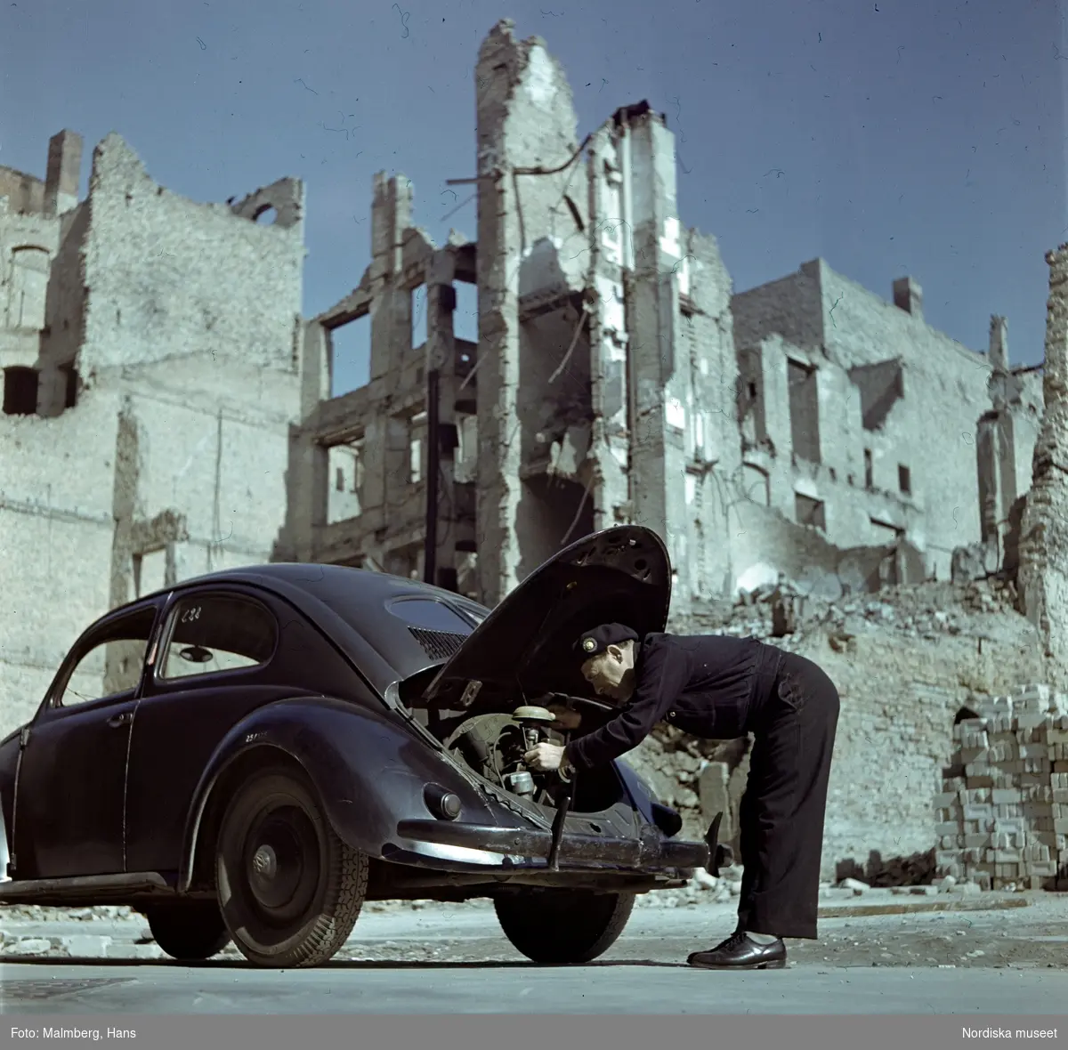 Berlin. En soldat ur de brittiska ockupationstrupperna kontrollerar motorn på en Volkswagen. Husruiner i bakgrunden.