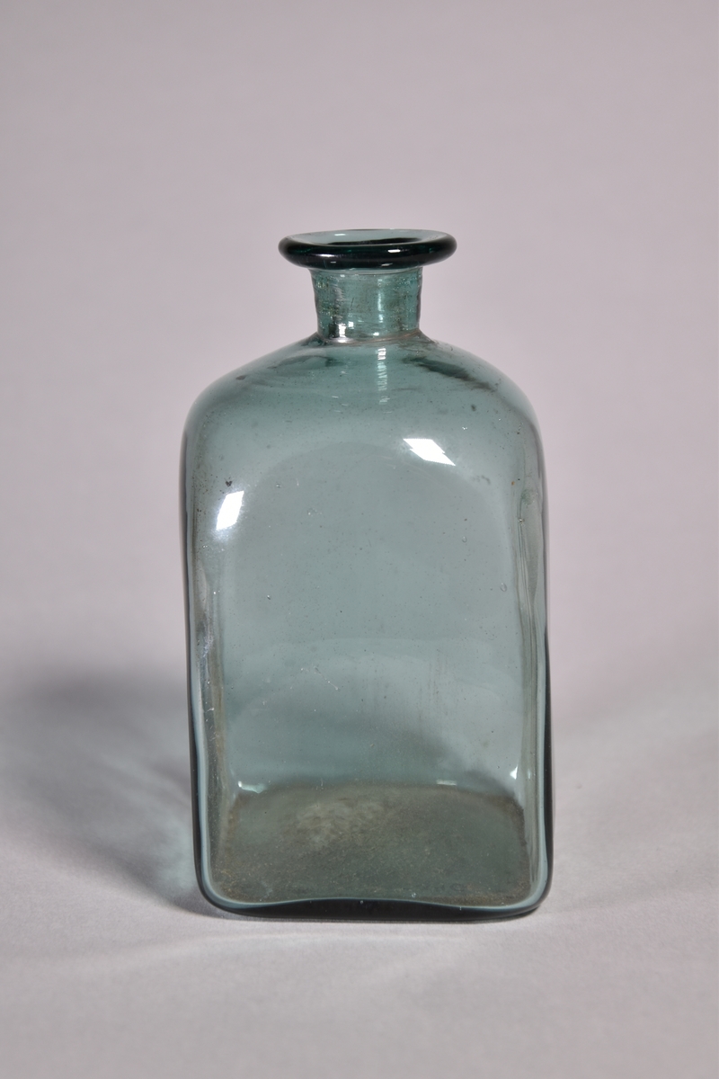 Flaska av grönt glas, kvadratisk, kort hals med utvikt mynning.
Spräckt.